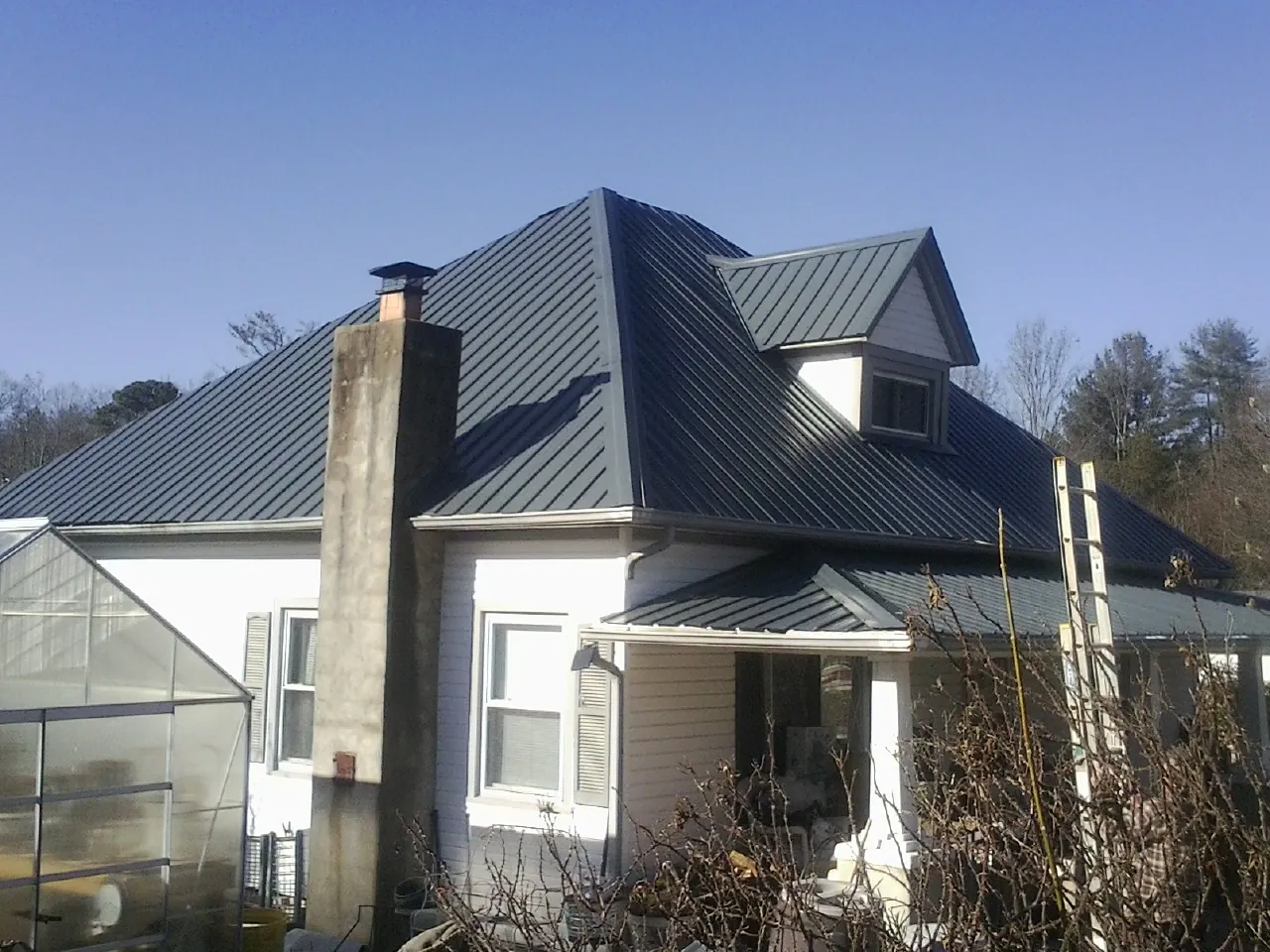 Dark blue standing seam metal roof on a white farmhouse with dormer — Slate & Tile Roof Repair by Roofing Brothers in Roberta