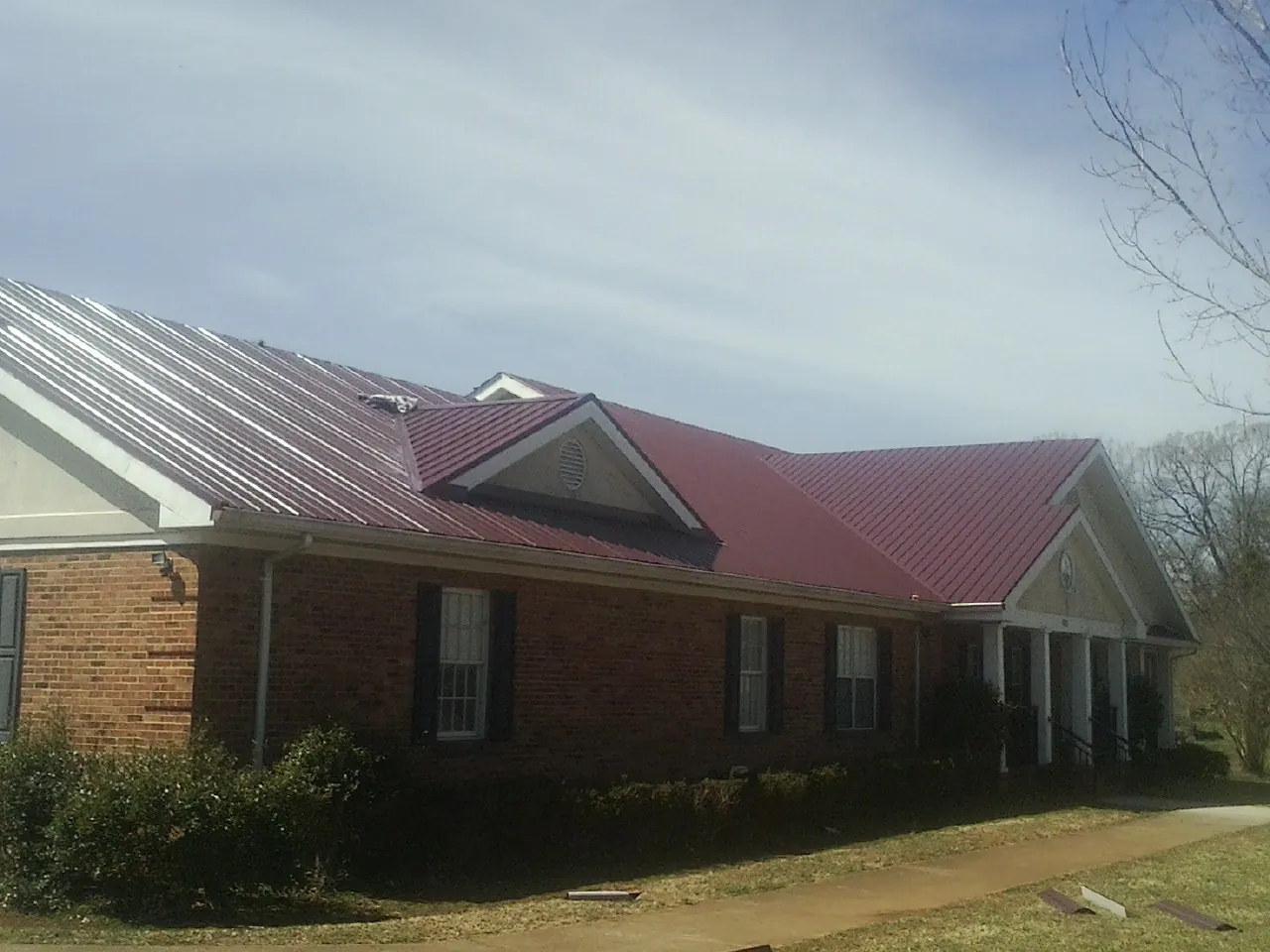Red metal roof with gabled entries on a long brick building, from a Hail Damage Roof Repair job in Roberta