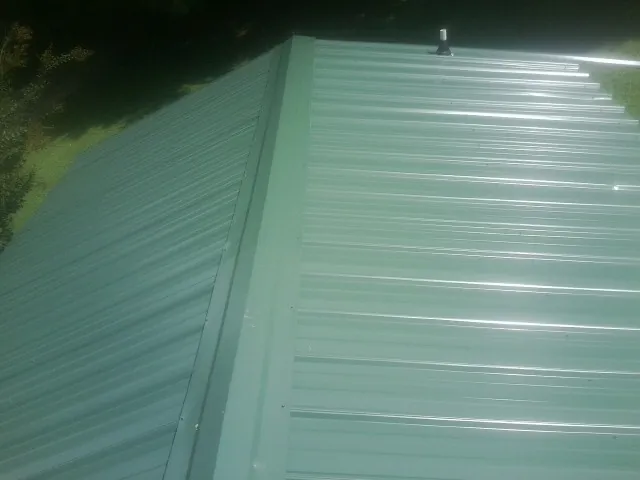 New green metal panels meeting at the ridge of a roof — Flat Roof Repair work by our crew in Roberta