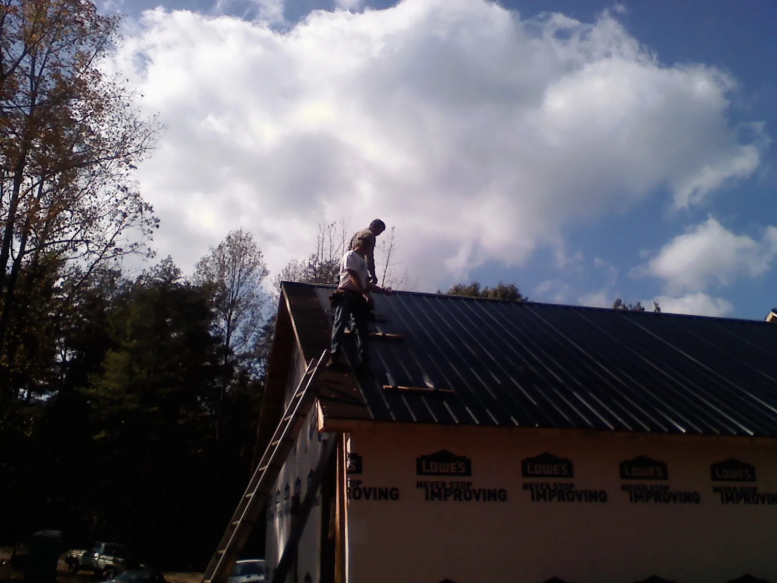 Roofer fastening dark metal panels high against a cloudy sky, from a Roof Inspection job in Roberta