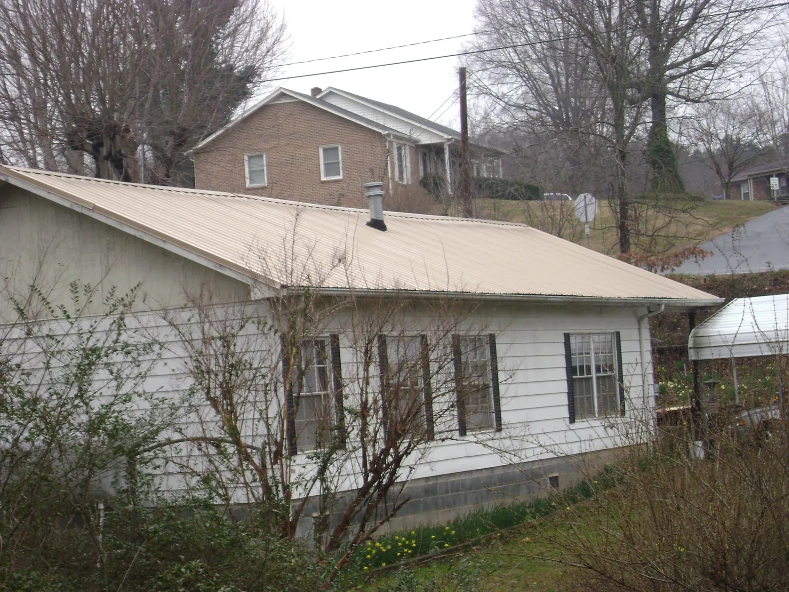 Tan metal roof on a white sided house set into a hillside — Commercial Roofing by Roofing Brothers in Roberta