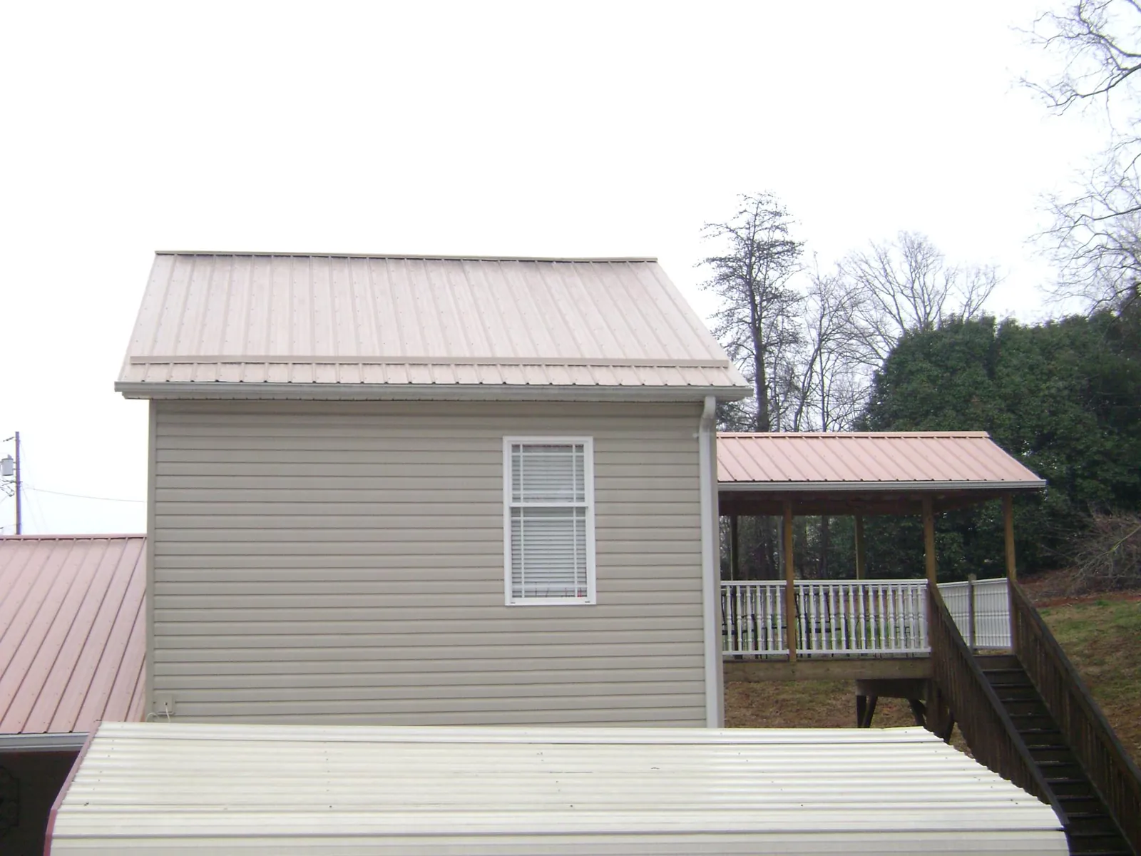 Tan metal roofs on a two story addition and attached porch, from a Roof Replacement job in Roberta
